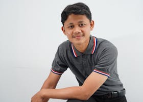 A confident young man in a casual shirt smiles warmly in a bright studio setting.