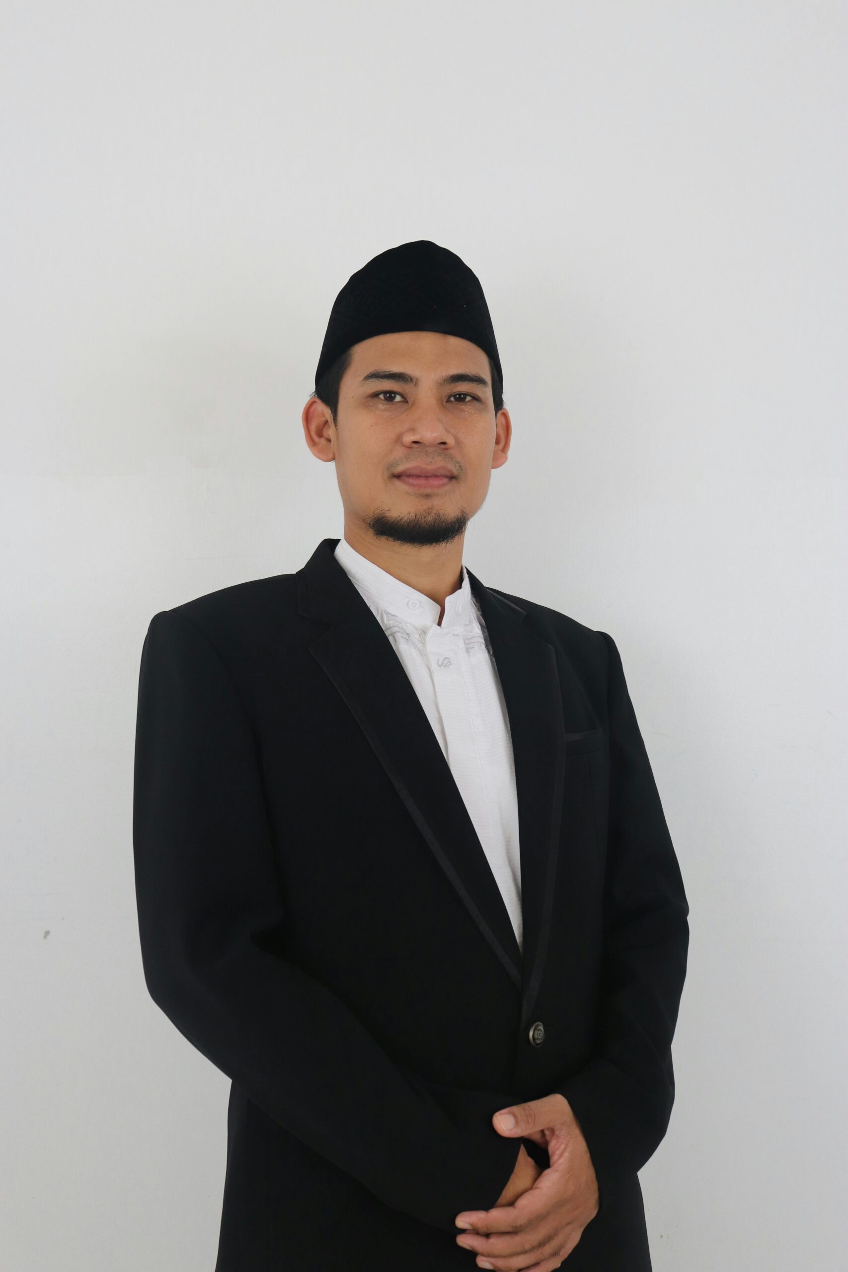 A confident man wearing a kufi and suit jacket, posing in front of a plain background.