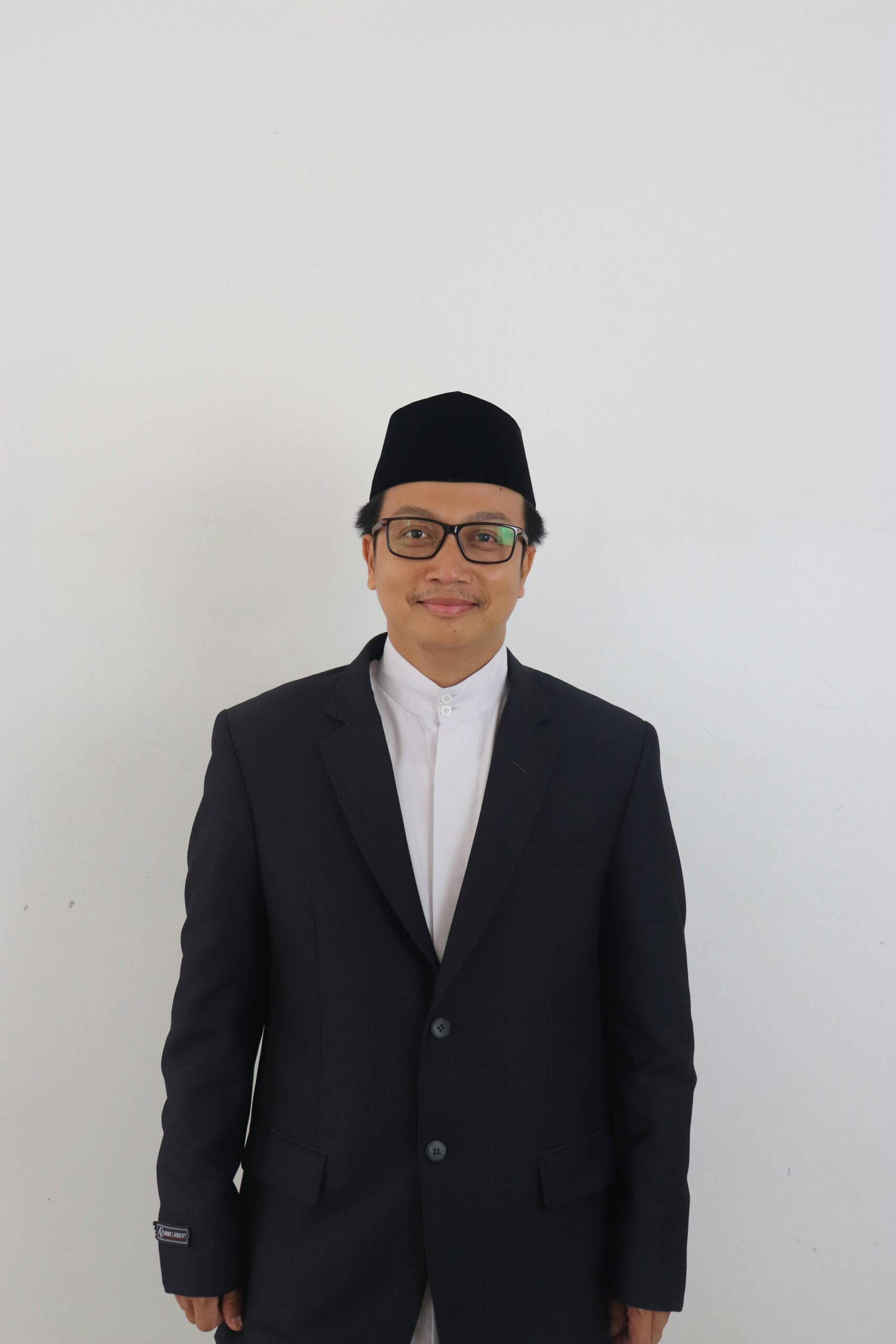 Portrait of a smiling man wearing a suit and kufi hat against a white background.